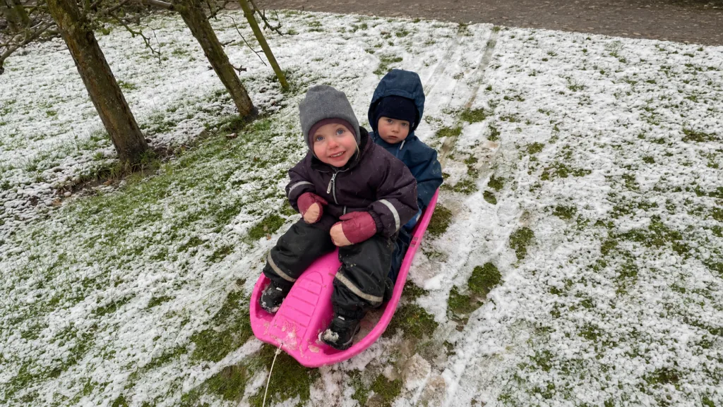 To små børn leger sammen på en pink kælk